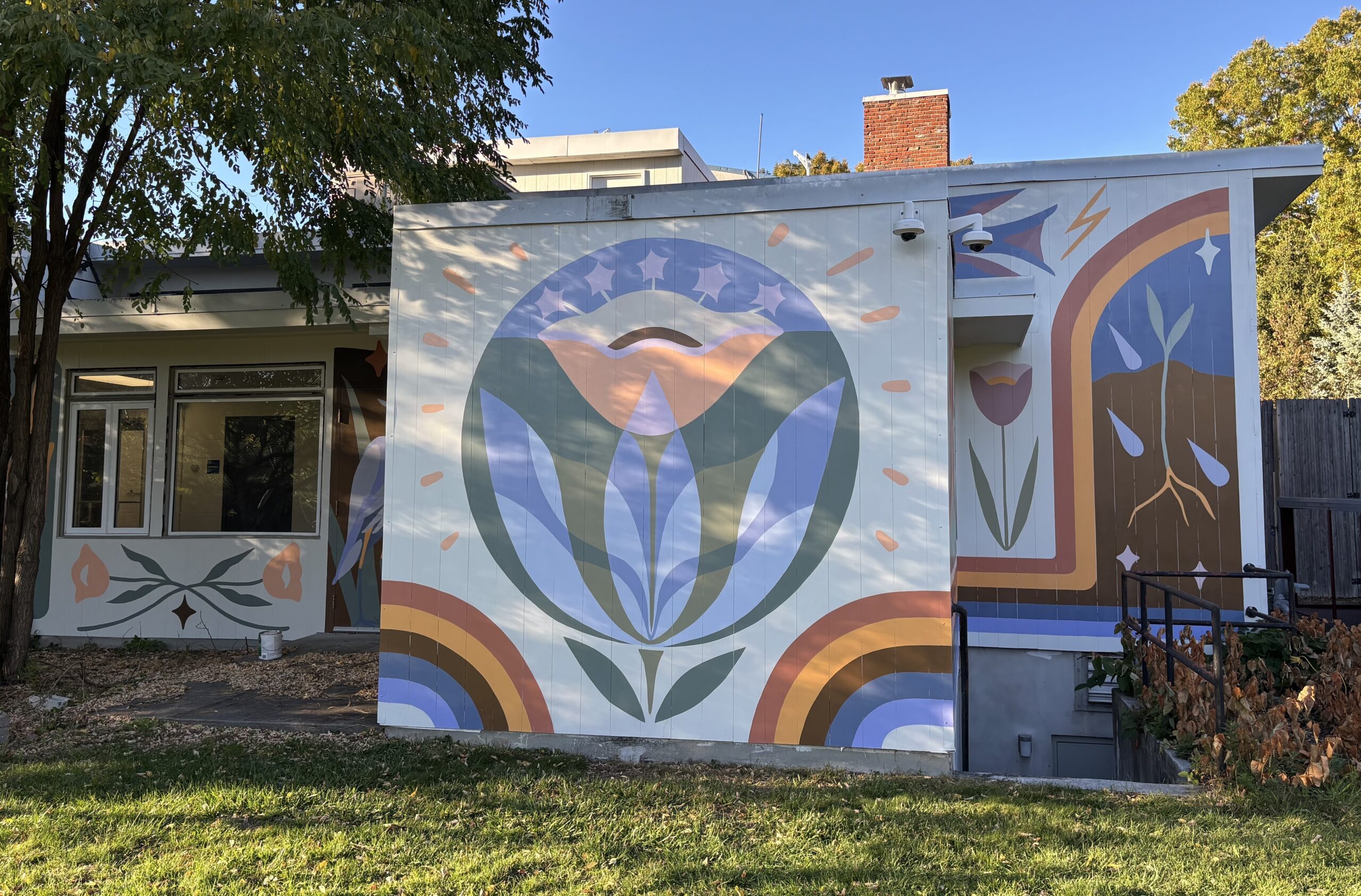 Mural on the Wayland Community Pool building with a large central flower and rainbow arches